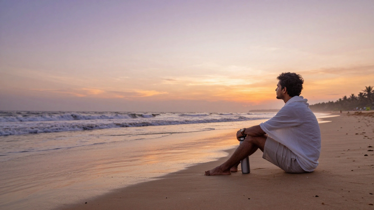A solo traveler sitting barefoot on an empty beach at sunset, wearing light clothing and holding a water bottle.